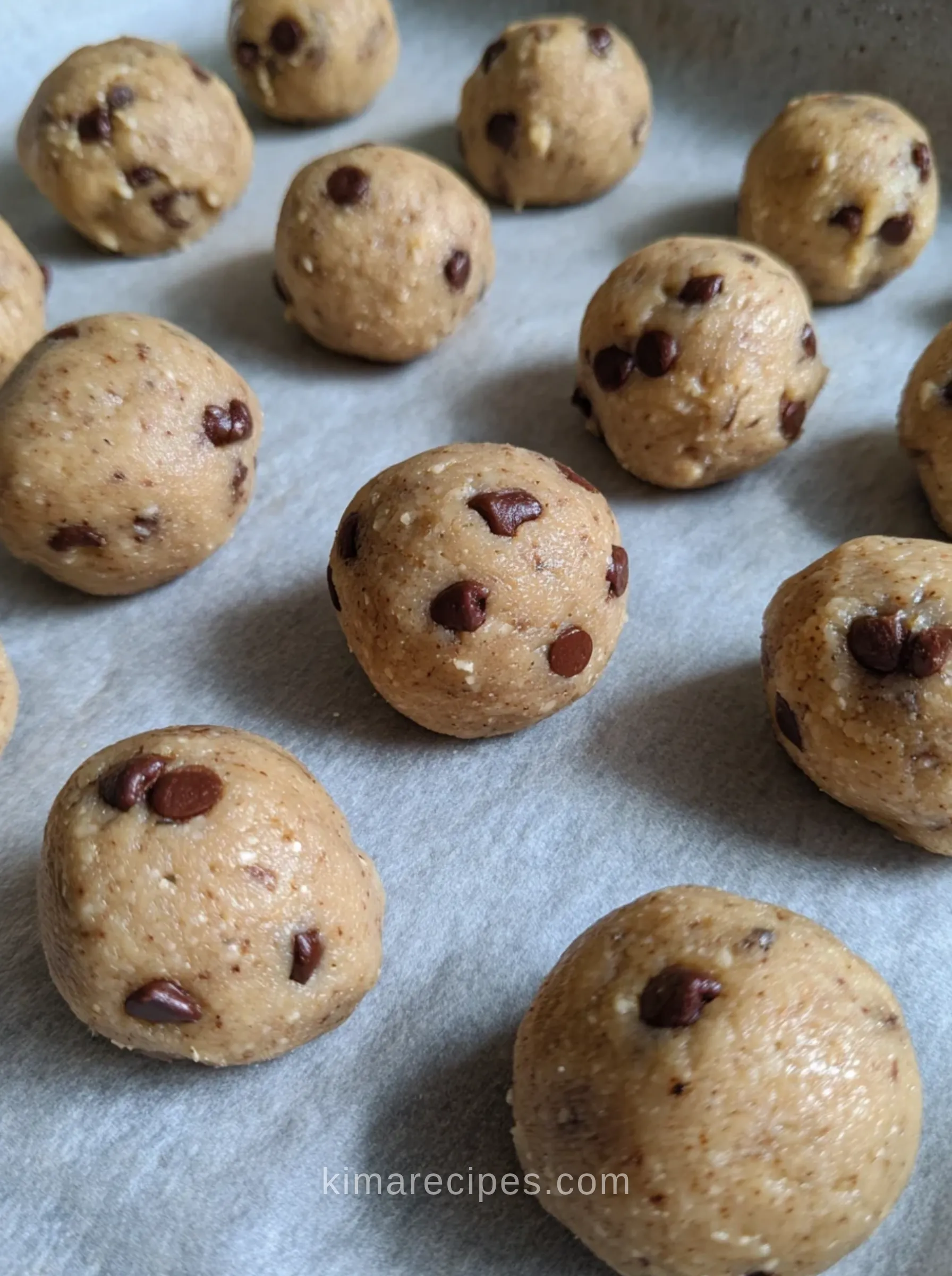 Rolled cookie dough protein bites with mini chocolate chips on parchment paper