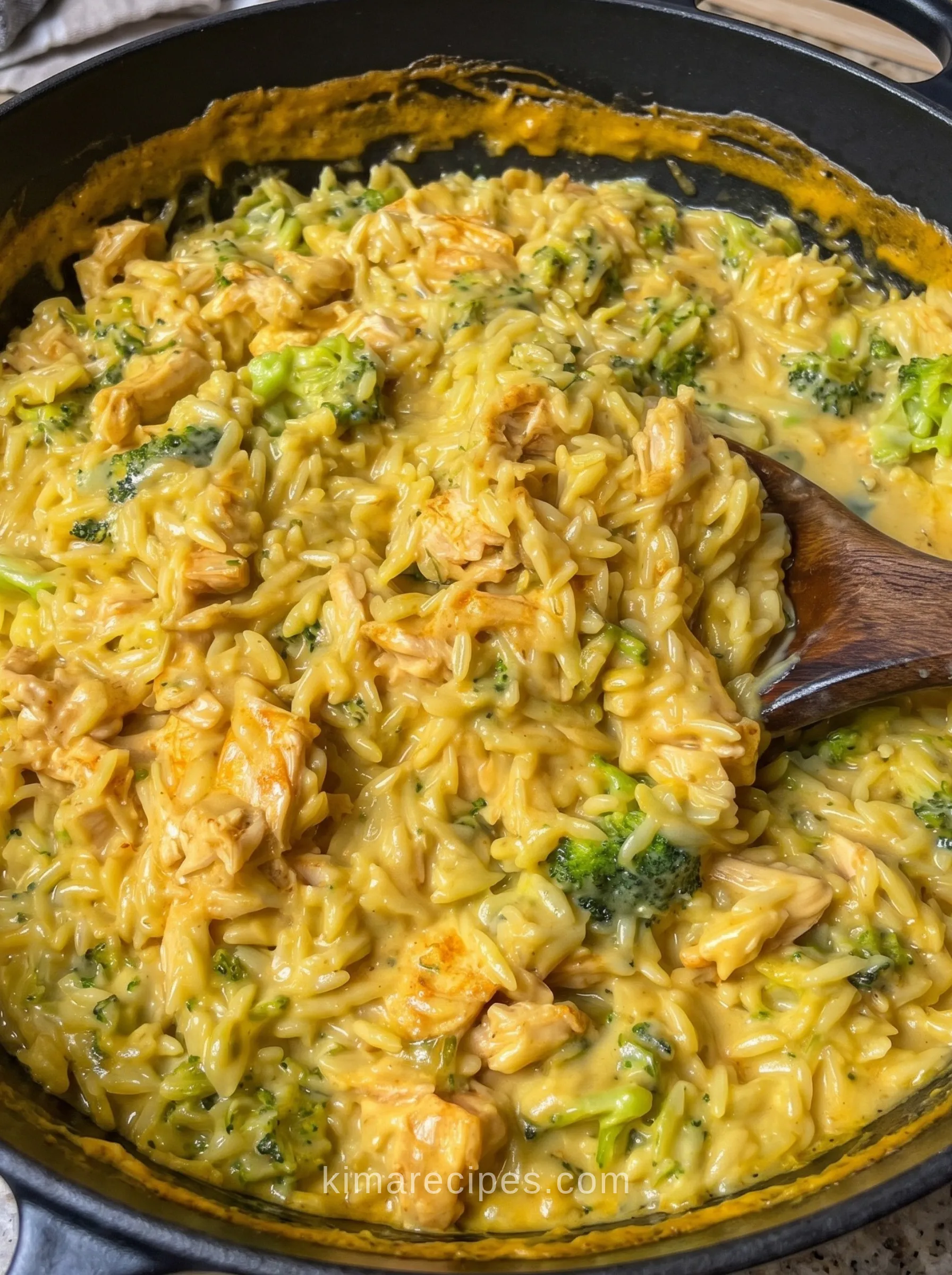 Creamy one-pan chicken broccoli orzo with melted cheddar in a black cast iron skillet with a wooden spoon