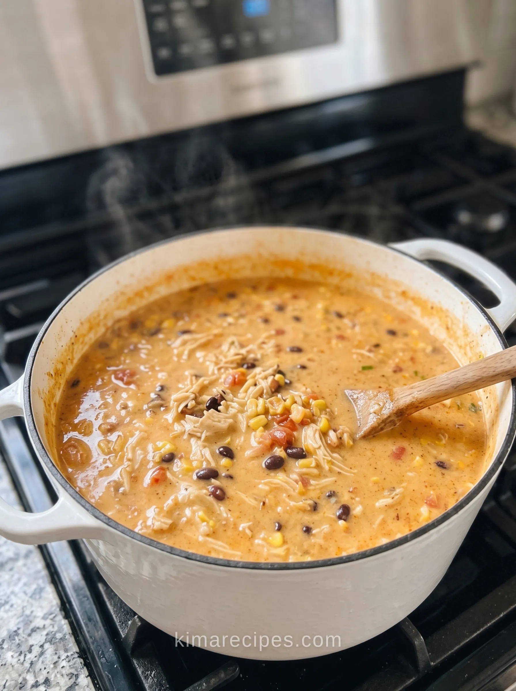Cheesy chicken enchilada soup simmering in a white Dutch oven with shredded chicken, black beans, corn, and a wooden spoon