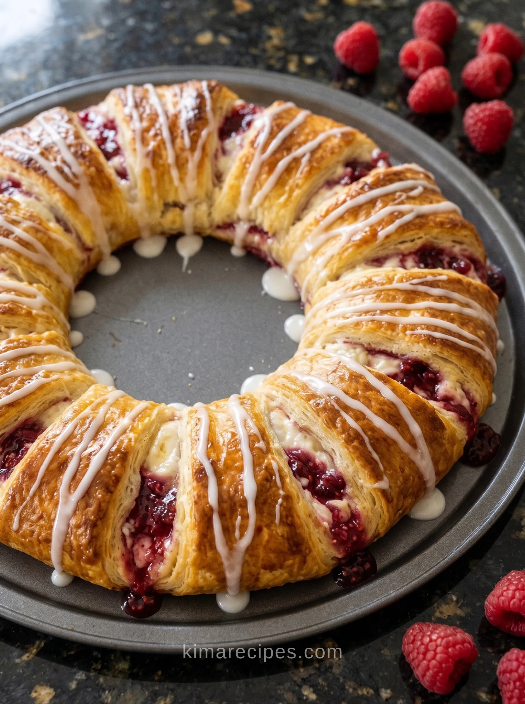 Raspberry cream cheese crescent ring with white glaze drizzle on a round pizza pan, fresh raspberries on the side