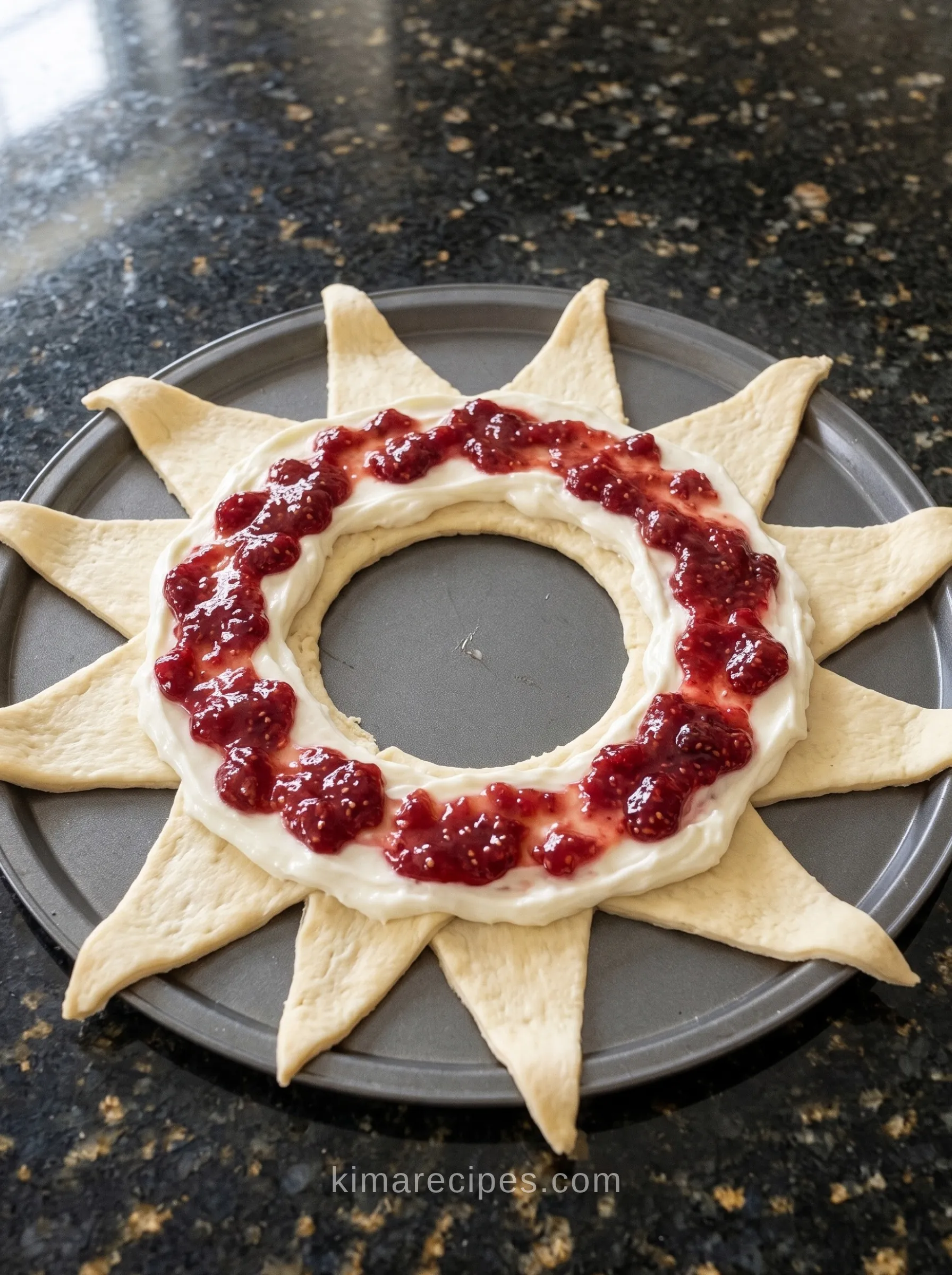 Unbaked raspberry cream cheese crescent ring: crescent dough triangles in a sunburst on a pizza pan, topped with a cream cheese band and a stripe of raspberry jam