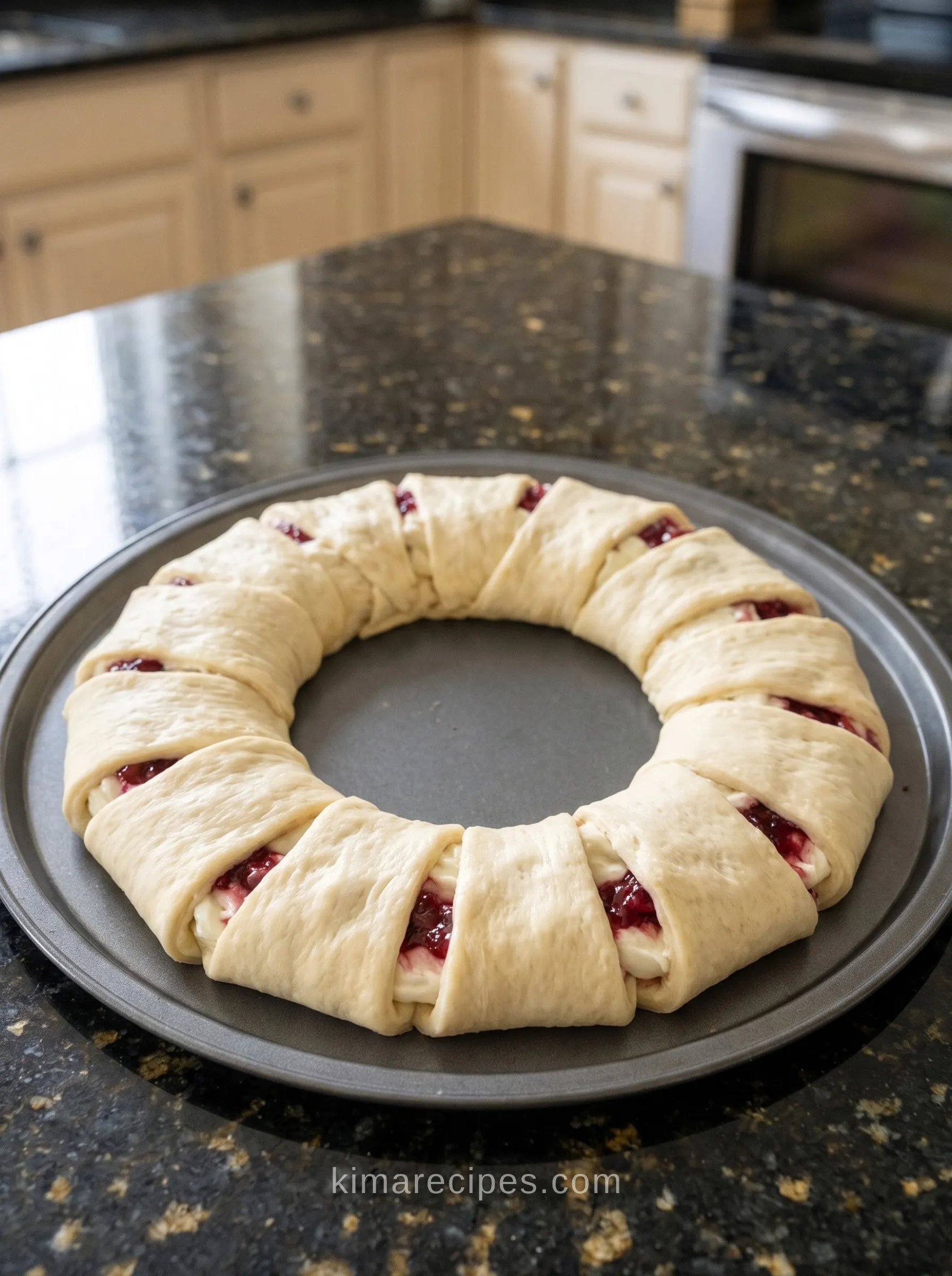 Unbaked raspberry cream cheese crescent ring on a pizza pan, crescent dough points folded over the cream cheese and raspberry jam filling