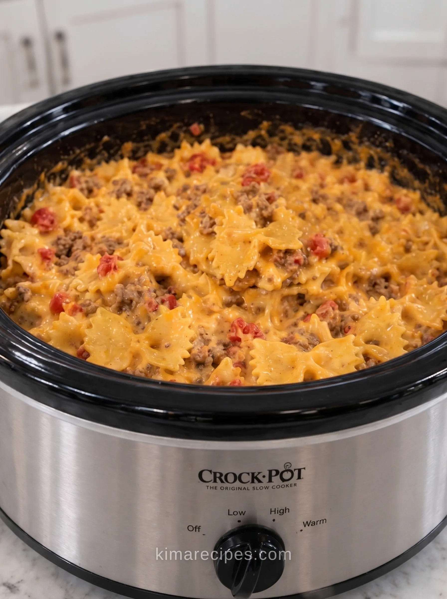 Cheesy taco bowtie pasta with ground beef and Rotel tomatoes finished in a stainless steel slow cooker