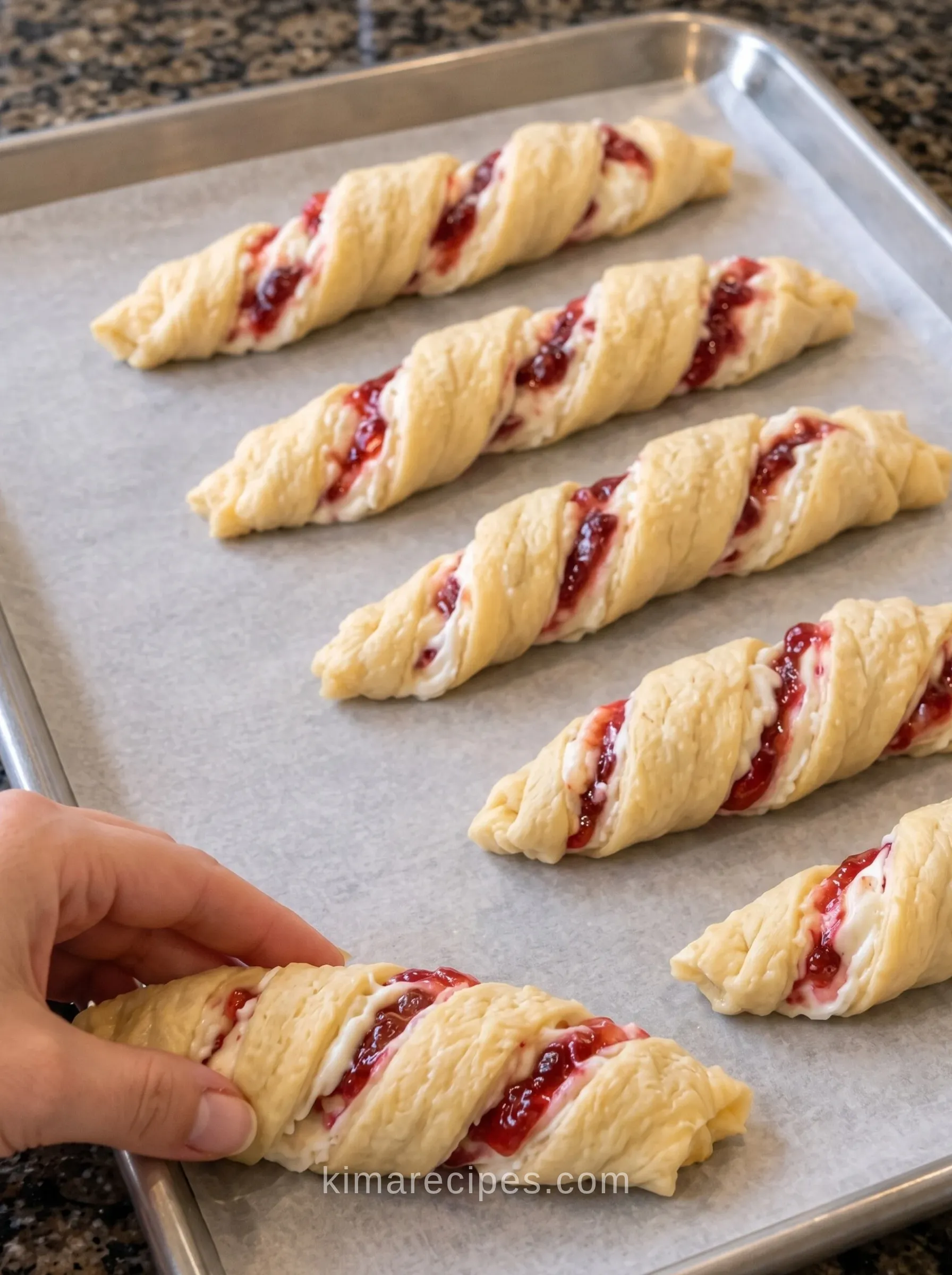 Rolled and twisted cheesecake strawberry crescent swirls with jam and cream cheese filling on a parchment-lined baking sheet before baking