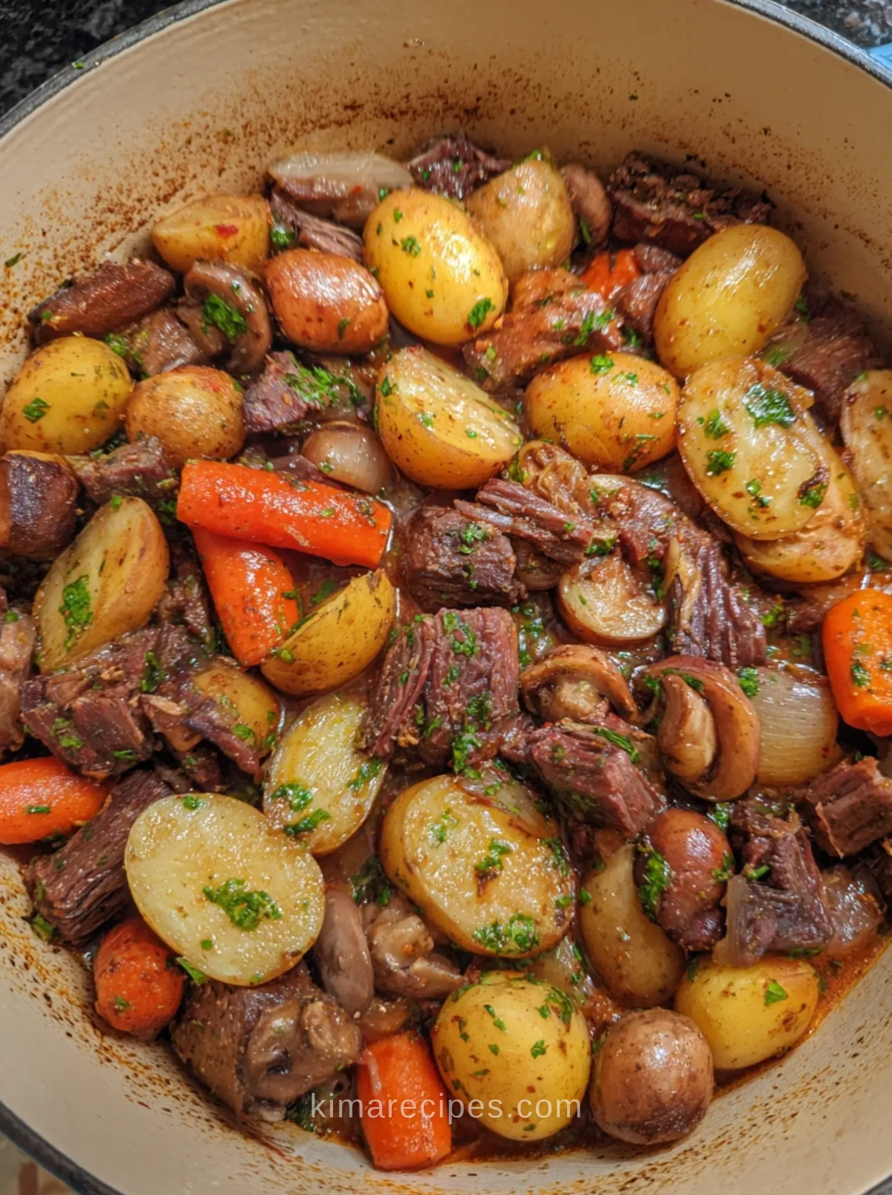Italian beef stew with baby potatoes, carrots, mushrooms and pearl onions in a Dutch oven, topped with parsley gremolata